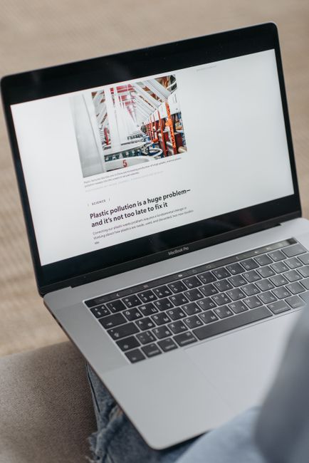 A silver MacBook Pro laptop placed on a person's lap, displaying a webpage with an image of a warehouse storage area filled with red and white shelving units and various stored items. The webpage feat